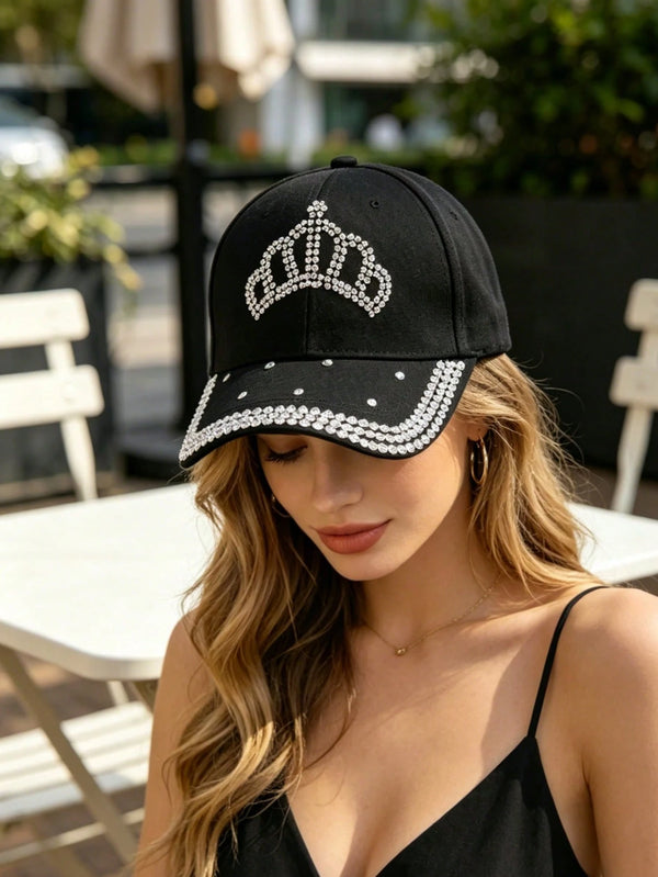 Woman wearing a black cap with a crown design and rhinestones outdoors.