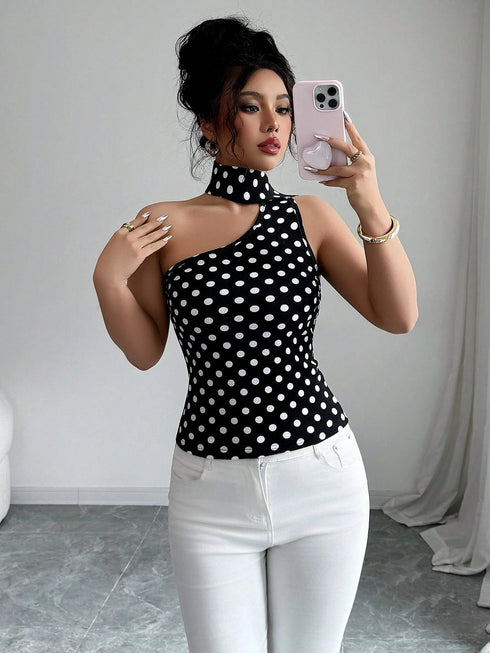 Woman taking a mirror selfie wearing a black polka dot top and white pants.