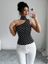 Woman taking a mirror selfie wearing a black polka dot top and white pants.