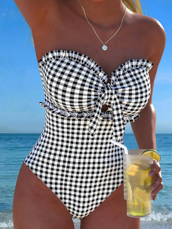 Woman in a black and white checkered swimsuit holding a drink with lemon slices against a beach background.