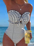 Woman in a black and white checkered swimsuit holding a drink with lemon slices against a beach background.