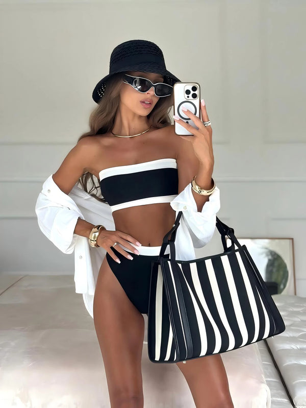 Woman in black and white outfit with striped bag taking a mirror selfie.