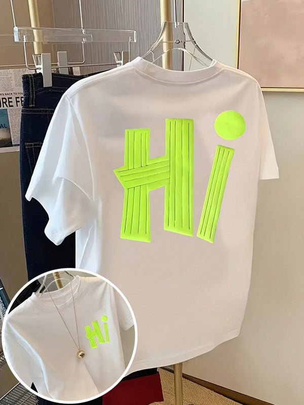 A white short-sleeve T-shirt hanging on a clear hanger, featuring a large neon yellow-green 3D block letter 'Hi' on the back with a matching neon yellow-green dot above it. A circular inset shows a close-up of the neon graphic on the front chest with a gold necklace worn over it.