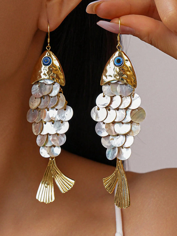 Gold fish-shaped earrings with circular components held by a hand.