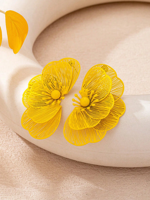 A pair of bright yellow flower-shaped earrings with fine textured petals and yellow centers, displayed on a curved cream-colored surface.