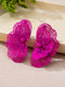 A pair of bright magenta-pink flower-shaped earrings with intricate wireframe petal detailing and small central spheres, displayed on a textured beige surface with a light stone slab in the background.