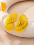 A pair of bright yellow flower-shaped earrings with fine textured petals and yellow centers, displayed on a curved cream-colored surface.