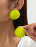 Close-up of a person wearing bright green earrings with a plain background