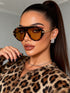 Woman wearing leopard print sunglasses and coat with a neutral background