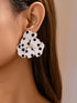 White floral earrings with black polka dots worn by a person.