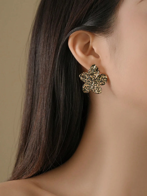 A close-up of a model's ear wearing a textured, flower-shaped gold earring with a leopard print pattern.