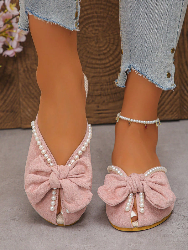 Pink suede shoes with bow and pearl details worn by a person.