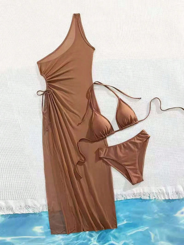 A brown swimwear set laid flat on a white textured surface with a blue water-patterned strip at the bottom. The set includes a one-shoulder maxi cover-up dress with side ties, a triangle bikini top, and matching bikini bottoms.