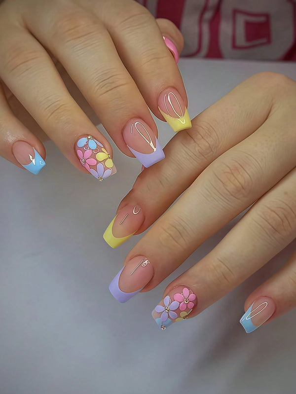 Close-up of a person's hands showcasing a pastel French manicure with floral nail art designs in pink, yellow, blue, and purple.