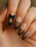 Close-up of a hand with manicured nails featuring a black and beige polka dot design, with one nail decorated in black with a glossy bow and another with small white pearl accents.