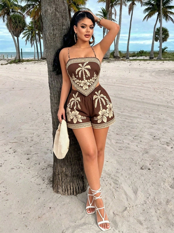 A woman posing on a sandy beach next to a palm tree, wearing a brown and beige tropical print two-piece romper with white strappy high-heeled sandals and holding a cream-colored woven bag.