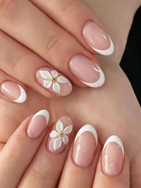 Close-up of manicured hands with a glossy French tip style and two white flower nail art designs with small gold centers.