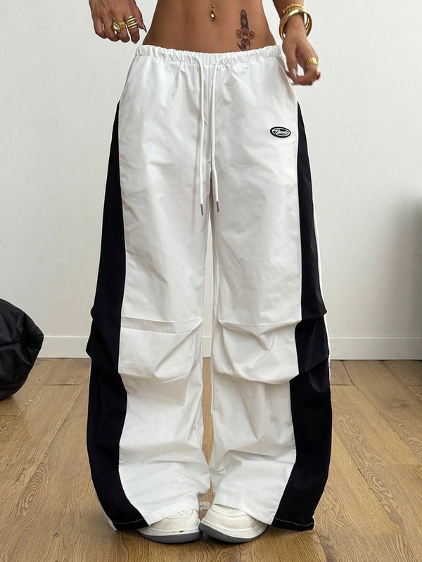 White pants with black side panels worn by a person on a wooden floor.