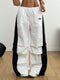 White pants with black side panels worn by a person on a wooden floor.