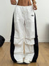 White pants with black side panels worn by a person on a wooden floor.