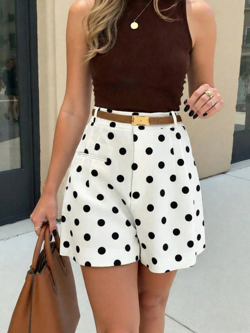 Woman wearing a brown top and white polka dot shorts with a tan handbag.