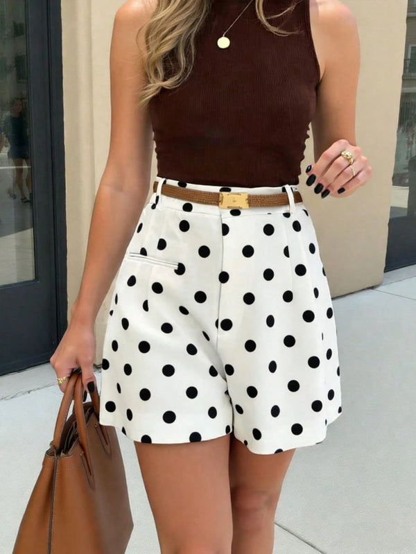 Woman wearing a brown top and white polka dot shorts with a tan handbag.