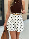 Woman wearing a brown top and white polka dot shorts with a tan handbag.