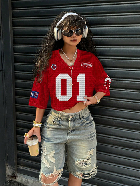 Person wearing a red sports jersey with number 01, denim shorts, and headphones, standing against a dark shutter.