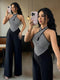A woman takes a mirror selfie wearing a sleeveless halter-style jumpsuit with a black and white striped geometric bodice and wide black legs. A second, larger view of the same outfit appears in the mirror background, showing the full length.