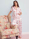 Woman wearing a white pajama set with red patterns, sitting on a floral armchair against a light blue wall.