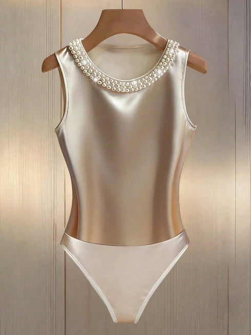 A sleeveless satin one-piece swimsuit in champagne beige with a pearl-trimmed neckline, displayed on a wooden hanger against a light wood-paneled background.