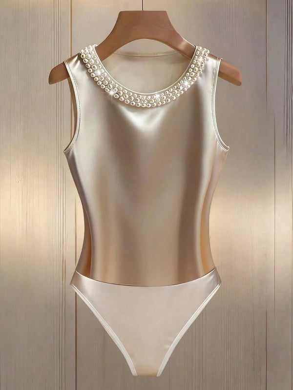 A sleeveless satin one-piece swimsuit in champagne beige with a pearl-trimmed neckline, displayed on a wooden hanger against a light wood-paneled background.