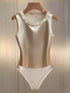 A sleeveless satin one-piece swimsuit in champagne beige with a pearl-trimmed neckline, displayed on a wooden hanger against a light wood-paneled background.
