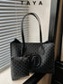 A black Taya tote bag with a repeating monogram pattern and a matching zip pouch, displayed on a windowsill with window blinds in the background.
