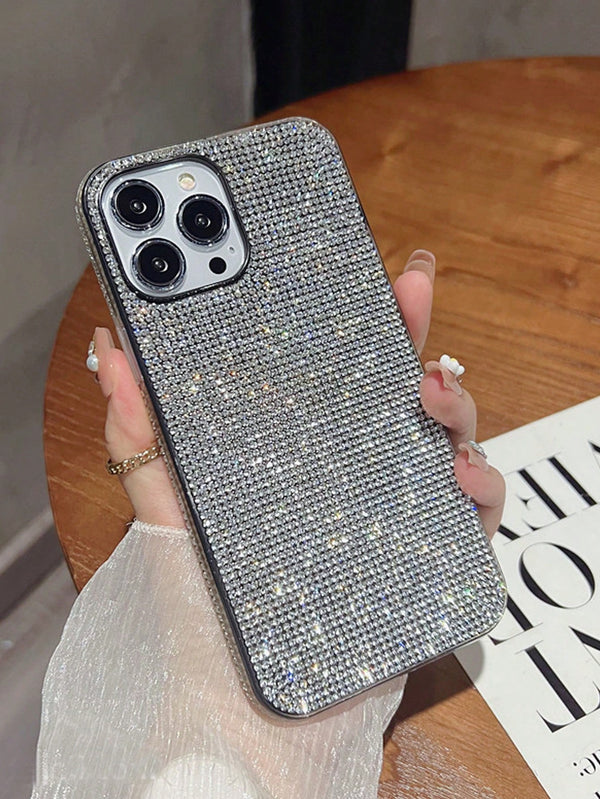 Silver glittery phone case held by a hand on a wooden surface with a magazine underneath.