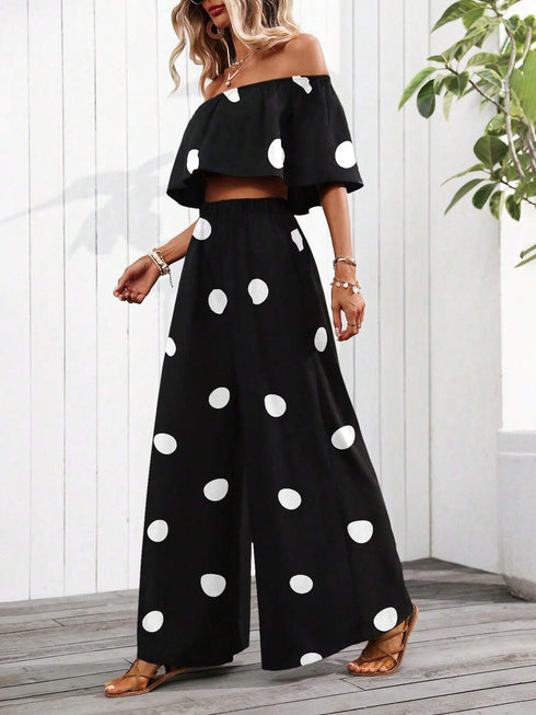 Woman wearing a black off-shoulder top and wide-leg pants with white polka dots, standing indoors.