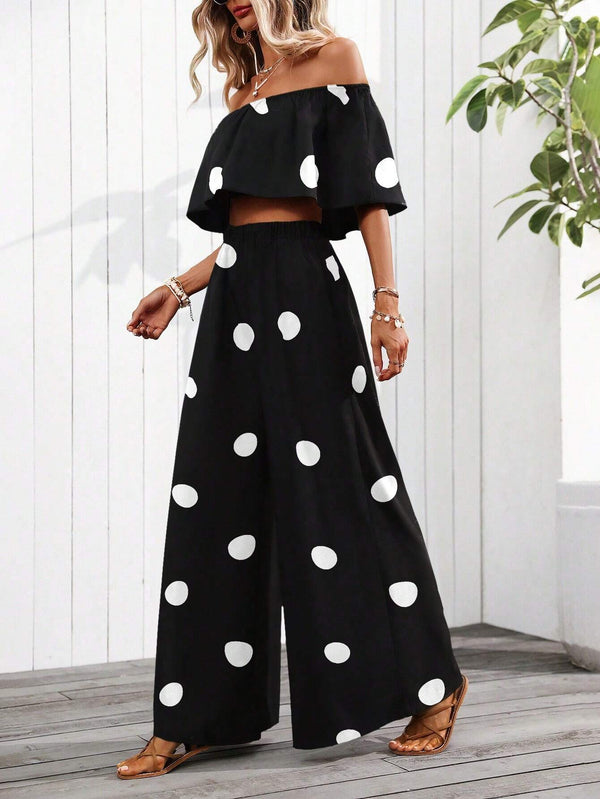 Woman wearing a black off-shoulder top and wide-leg pants with white polka dots, standing indoors.