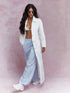Woman wearing a white coat, light blue pants, and white sneakers on a pink background