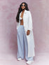 Woman wearing a white outfit with a long white coat against a pink background