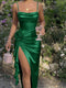 Woman in a green dress holding a glass and a small bag, standing in a natural setting with flowers and rocks.