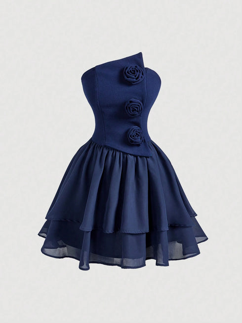 A navy blue one-shoulder dress with a structured corset-style bodice, three dimensional fabric roses on the front, and a layered ruffled skirt, shown against a light gray background.