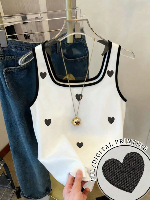 White tank top with black heart patterns on a hanger, with jeans in the background.