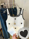 White tank top with black heart patterns on a hanger, with jeans in the background.