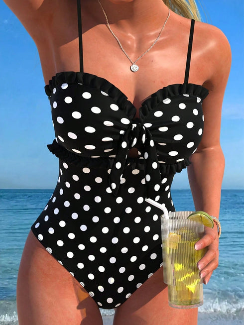 Woman in a black polka dot swimsuit holding a drink by the beach