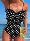 Woman in a black polka dot swimsuit holding a drink by the beach
