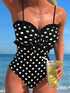 Woman in a black polka dot swimsuit holding a drink by the beach