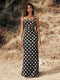 Woman wearing a black polka dot dress standing in a natural setting.