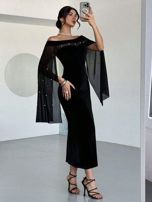 A woman takes a mirror selfie wearing a black off-the-shoulder midi dress with sheer flutter sleeves adorned with small silver studs, paired with black strappy high-heeled sandals.