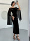 A woman takes a mirror selfie wearing a black off-the-shoulder midi dress with sheer flutter sleeves adorned with small silver studs, paired with black strappy high-heeled sandals.