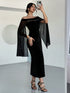 A woman takes a mirror selfie wearing a black off-the-shoulder midi dress with sheer flutter sleeves adorned with small silver studs, paired with black strappy high-heeled sandals.